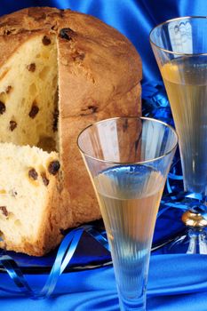 Panettone the italian Christmas fruit cake served on a blue glass plate over a blue fabric background and two glasses of spumante (sparkling wine). Selective focus.