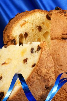 Panettone the italian Christmas fruit cake over a blue fabric background and blue ribbons. Selective focus.