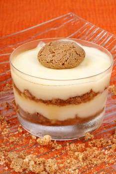 Close-up of vanilla custard and amaretti dessert served in a glass cup over an orange background. Selective focus.