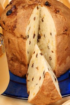 Panettone the italian Christmas fruit cake served on a blue glass plate over a yellow background and a glass of spumante (sparkling wine). Selective focus.