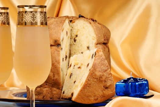 Panettone the italian Christmas fruit cake served on a blue glass plate over a yellow background and two glasses of spumante (sparkling wine). Selective focus.