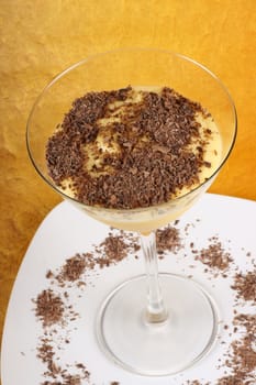 Vanilla custard cream with chocolate dessert served in a glass over a white plate.