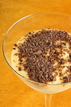 Vanilla custard cream with chocolate dessert served in a glass over an orange background. Selective focus.