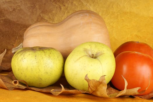 Autumn still life composition with pumpkin, apples and persimmon fruits over sycamore leaves.