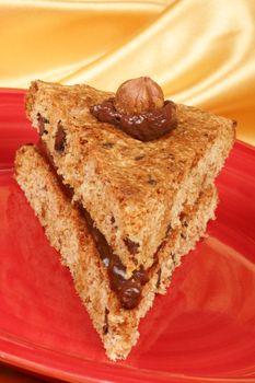 Slice of hazelnut and chocolate cake served on a red dish over a yellow background.