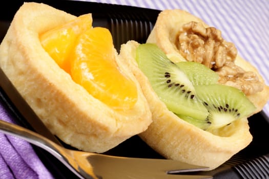 Close-up of some mini fruit tarts served on a black plate with dessert fork. Selective focus.