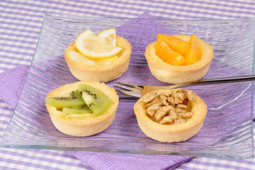 Close-up of some mini fruit tarts served on a glass plate with dessert fork. Selective focus.