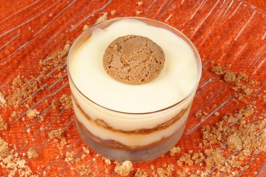 Close-up of vanilla custard and amaretti dessert served in a glass cup over an orange background. Selective focus.