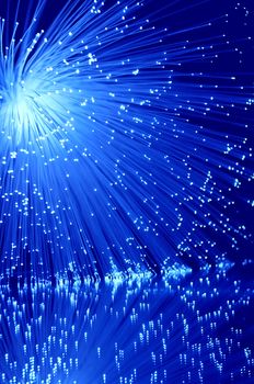 Vibrant blue illuminated fibre optic light strands against blue background and reflecting into the foreground.