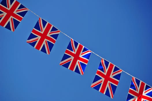 A line of Union ack flagy, stetched across a clear blue sky. Space for text either side of the flags