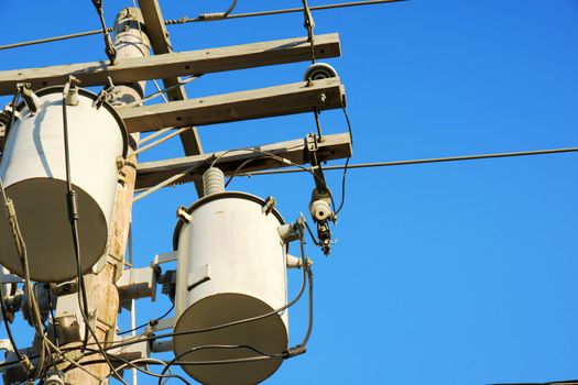 Close up of electricity transformers up in power line post, against blue sky.