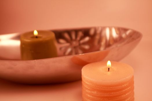 Two lit candles next to a shiny metallic dish. Dish has white mother of pearl decorative accents. Home decor and interior design decoration.