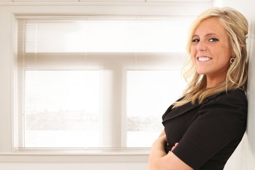 Beautiful young blond woman standing in front of window at office or school.  Space for copy.
