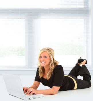 Beautiful young woman working on laptop in school or office on floor with copy space.