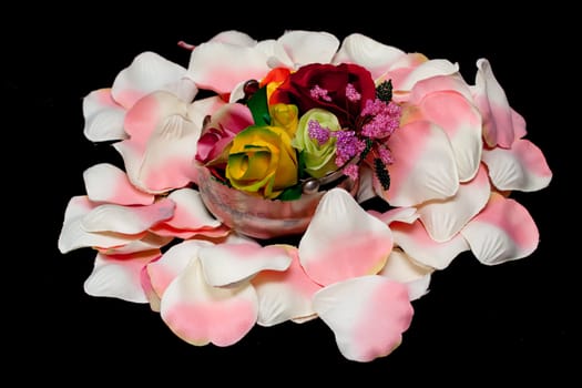 A silver basket with artificial roses on white and pink rose textile petals on black
