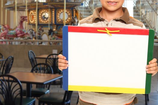 Young boy holding blank dry erase board in the food court of a mall.
