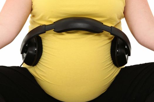 Beautiful pregnant 23 year old american woman with headphones on belly over white.