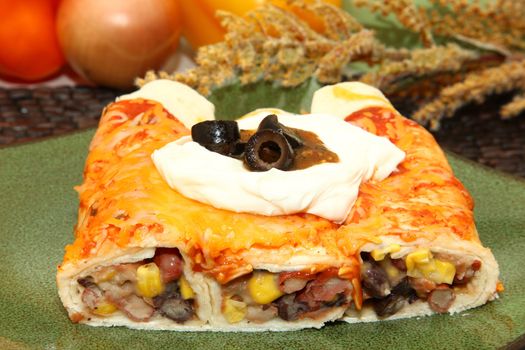 Plate with three bean enchilada with melted cheese, sour cream, tomatillo sauce and olives.  Kidney beans, pinto beans, black beans and corn inside.