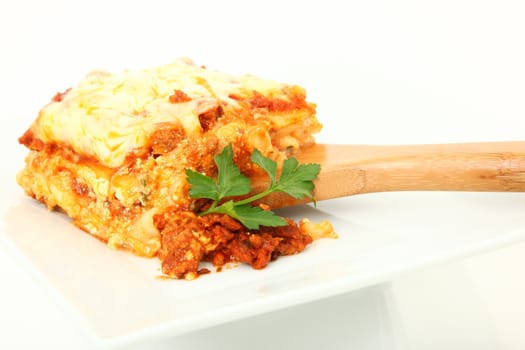 Square of baked lasagna with parsley on bamboo serving spoon