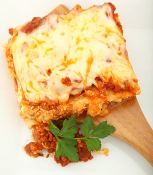 Square of baked lasagna with parsley on bamboo serving spoon