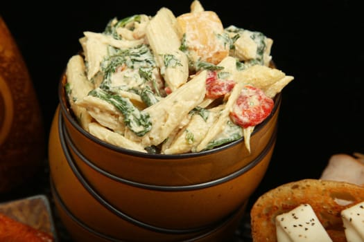 Pasta salad with spinach, red bell peppers, chicken, in bowl.