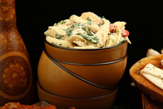 Pasta salad with spinach, red bell peppers, chicken, in bowl.