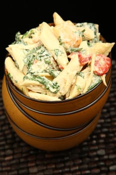 Pasta salad with spinach, red bell peppers, chicken, in bowl.