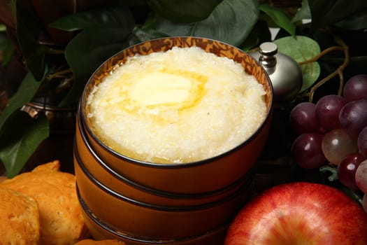 Bowl of hot grits and butter with biscuits and fruit in kitchen.