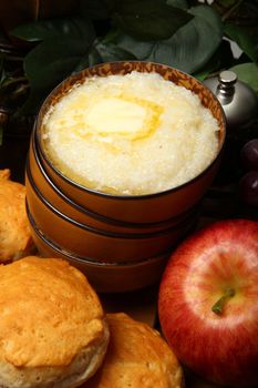 Bowl of hot grits and butter with biscuits and fruit in kitchen.