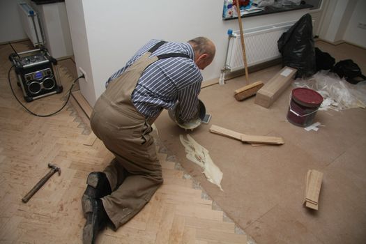 Man laying a wooden parquetry flooring by putting glue first before nailing wooden panels one by one