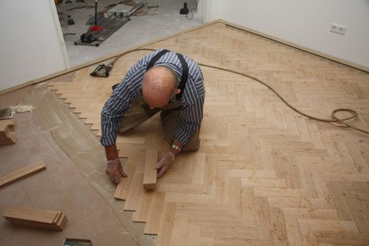 Man laying a wooden parquetry flooring in fishbone pattern
