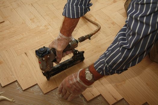 Detail of a man busy laying a wooden floor in fishbone pattern