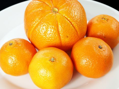 Orange and clementine on white plate towards black background