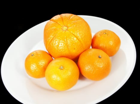 Orange and clementine on white plate towards black background