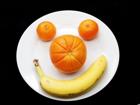 Orange, clementine and banana isolated on white plate towards dark background