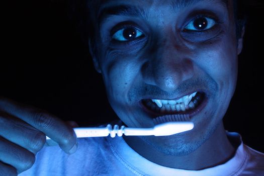 An Indian vampire brushing his teeth with a white toothbrush.