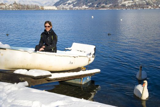 Young woman sitting in boat in Zell am See, Austria with swans swimming beside her.