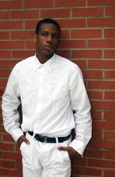 A man dressed in white standing by brick wall