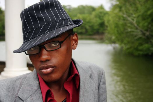 A man with a hat and glossy lips in front of a lake