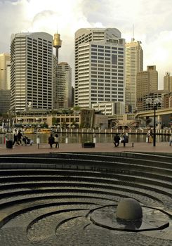 grey photo of Darling Harbour, Sydney Tower in background, modern fountain in foreground