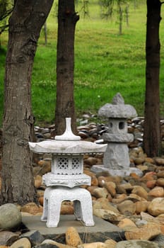small buddhist sculptures made of stone, small stones, green grass, and trees in background
