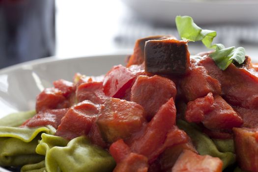 Close up of spinach tortellini covered in tomato sauce with aubergine.
