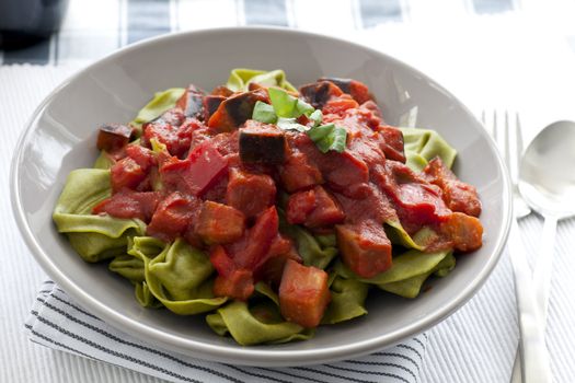 Spinach tortellini covered in tomato sauce with aubergine.