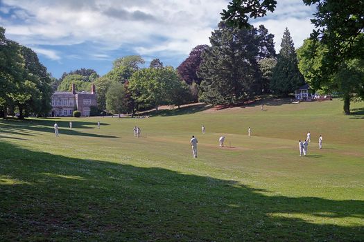 Cricket is often played on village greens, sometimes as here, close by the former  Squire's abode. This game is taking place at Cockington in Devon, England.