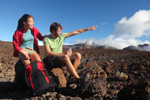 Young couple outdoors hikers looking at view pointing at copy space. Mixed race couple (asian and caucasian) on hiking trip in volcanic landscape, Teide, Tenerife, Canary Islands, Spain.