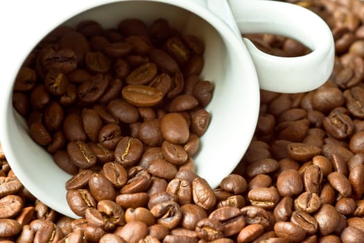 A white cup surrounded and partly filled with coffee beans