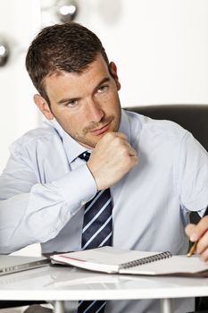 young pensive businessman in office with pen