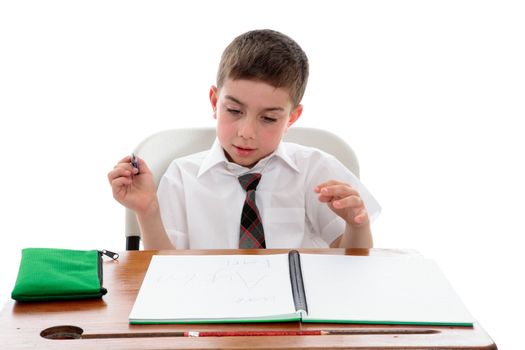 A school boy at a desk with book He is reading and examining his writing.  White background.