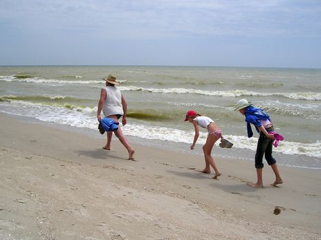 The father unhurriedly by wide step goes in front along the coast of sea, and two girls try to go on his tracks. 