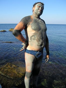 man was smeared by useful therapeutic mud on the shore of Azov sea in order to obtain therapeutic effect. Mud gradually dries in the sun, and it then washes off by water.